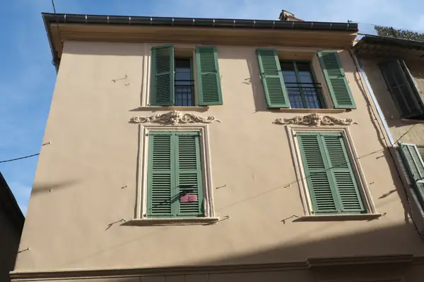 Façade enduite ocre clair à Vence, volets persiennés verts et encadrements moulurés